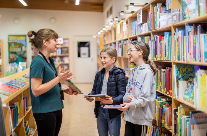 Bibliotekarie ger bokförslag till två tjejer.