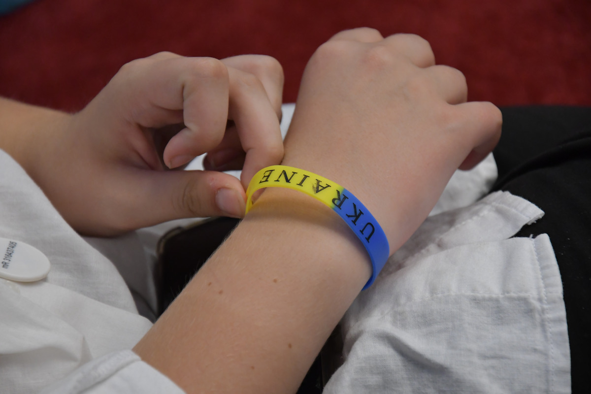 Två händer med ett armband i gult och blått med texten Ukraine