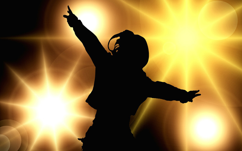 En mörk siluett av en person som dansar med armarna utsträckta med strålkastare i bakgrunden.