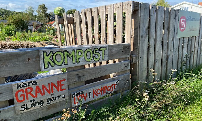Trälåda för kompost med skylt som välkomnar grannar att slänga löv och kompost.